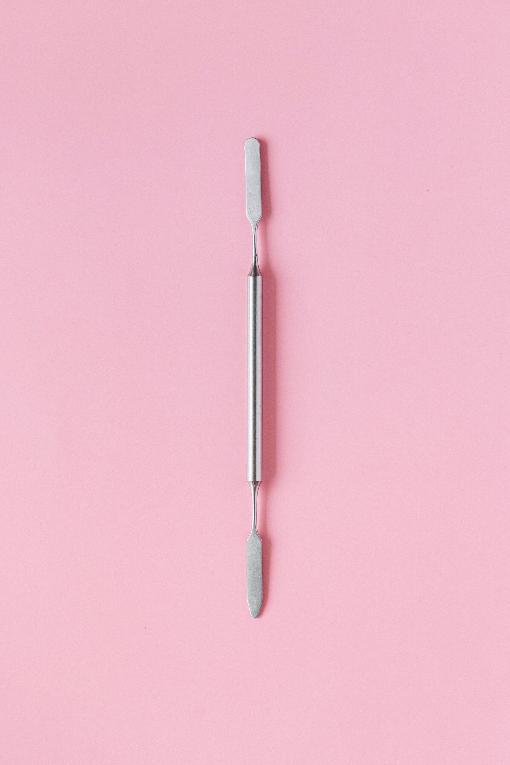 Minimalist image of a stainless steel tool on a pink background, top view.